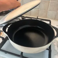 Customer-uploaded image. Click to see more details. The image represents: A hand lifting the lid of a white ceramic pot with black interior sitting on a gas stovetop in a kitchen