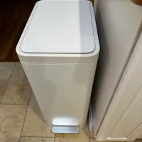Customer-uploaded image. Click to see more details. The image represents: White rectangular step-on trash can with lid positioned next to kitchen cabinets on tiled floor