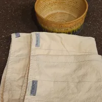Customer-uploaded image. Click to see more details. The image represents: A wooden bowl sits next to folded white cloth napkins with blue labels on a dark speckled countertop