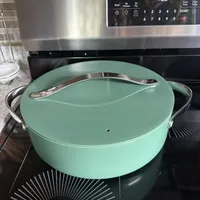 Customer-uploaded image. Click to see more details. The image represents: A mint green Dutch oven with lid and handles sitting on a black stovetop in front of a stainless steel microwave