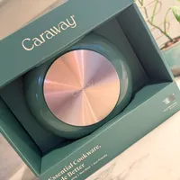 Customer-uploaded image. Click to see more details. The image represents: Caraway brand cookware product box displayed open, showing a round pan with rose gold metallic bottom and teal-colored rim, packaged in a matching teal box labeled "Essential Cookware Made Better" with eco-friendly messaging.