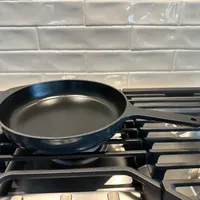 Customer-uploaded image. Click to see more details. The image represents: A black frying pan sits on a gas stove burner against a white subway tile backsplash in a kitchen