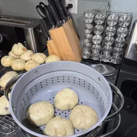 Customer-uploaded image. Click to see more details. The image represents: Kitchen counter with steamer basket containing potatoes, knife block, spice rack, and other cooking equipment