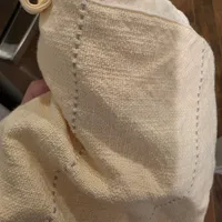 Customer-uploaded image. Click to see more details. The image represents: A beige burlap or linen drawstring bag with decorative stitching along the edges, held in someone's hand