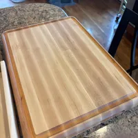 Customer-uploaded image. Click to see more details. The image represents: A large wooden cutting board with natural wood grain sits on a granite kitchen countertop
