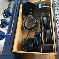 Customer-uploaded image. Click to see more details. The image represents: Open kitchen drawer with organized cookware including pots, pans, and a colander stored in wooden compartments