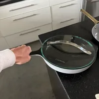 Customer-uploaded image. Click to see more details. The image represents: Person holding a white ceramic pan with glass lid on a dark granite kitchen countertop