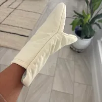 Customer-uploaded image. Click to see more details. The image represents: Person wearing cream-colored sock with foot raised, sitting in bright room with tiled floor and plants in background