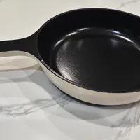 Customer-uploaded image. Click to see more details. The image represents: A black and cream enameled cast iron skillet with a long handle, placed on a marble countertop with natural lighting casting shadows.