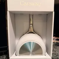 Customer-uploaded image. Click to see more details. The image represents: A white Caraway brand frying pan with gold handle displayed in its retail packaging box on a granite countertop