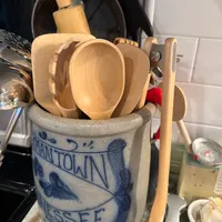 Customer-uploaded image. Click to see more details. The image represents: A kitchen counter display showing wooden cooking utensils and bowls stored in a decorative blue and white ceramic crock with text reading "Tennessee." Wooden spoons and spatulas are visible, along with kitchen items in the background including a dark pan and white subway tile backsplash.