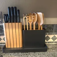 Customer-uploaded image. Click to see more details. The image represents: A kitchen counter organizer with two sections: the left side holds kitchen knives with black handles in a light wood block, and the right side contains wooden cooking utensils including spoons and spatulas in a black container. The organizer sits on a granite countertop with a decorative tile backsplash.