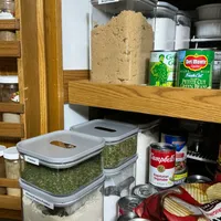 Customer-uploaded image. Click to see more details. The image represents: Organized pantry shelves with labeled storage containers holding brown sugar, parsley, and almond protein powder, alongside canned goods including Del Monte green beans and Campbell's soup