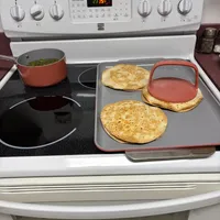 Customer-uploaded image. Click to see more details. The image represents: Kitchen stove with flatbreads cooking on a baking sheet and a pot with green vegetables on the burner