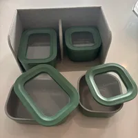 Customer-uploaded image. Click to see more details. The image represents: Four green silicone watch cases with clear windows displayed in a gray fabric storage box and on a white surface.
