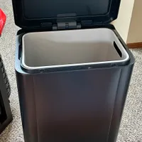 Customer-uploaded image. Click to see more details. The image represents: A black rectangular trash can with a hinged lid open, showing a gray interior liner and a small pedal at the base for hands-free operation.