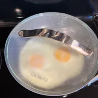 Customer-uploaded image. Click to see more details. The image represents: A Caraway brand glass pot lid containing two eggs cooking in clear liquid or broth on a stovetop.