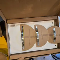 Customer-uploaded image. Click to see more details. The image represents: An open cardboard box containing three tan-colored circular cookware lids with stainless steel handles, arranged in a row on white protective packaging material.