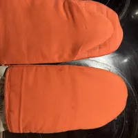 Customer-uploaded image. Click to see more details. The image represents: Orange oven mitts placed on a black stovetop surface