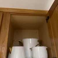 Customer-uploaded image. Click to see more details. The image represents: White ceramic pots and containers with gold handles stored inside an open wooden kitchen cabinet