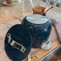 Customer-uploaded image. Click to see more details. The image represents: A dark blue teapot with lid removed sits on a wooden cutting board next to a glass tea brewing vessel on a kitchen counter