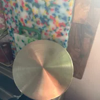 Customer-uploaded image. Click to see more details. The image represents: A circular brushed metal surface with concentric rings reflecting warm light, with colorful artwork visible in the background