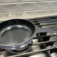Customer-uploaded image. Click to see more details. The image represents: A black non-stick frying pan sitting on a gas stove burner with white subway tile backsplash in the background