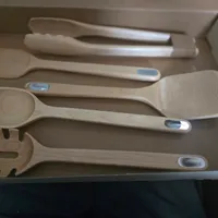 Customer-uploaded image. Click to see more details. The image represents: A set of wooden kitchen utensils in a cardboard box, including spoons, spatulas, and a pasta server with blue branded labels on the handles.