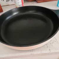 Customer-uploaded image. Click to see more details. The image represents: A black non-stick skillet or frying pan with a light pink exterior handle, sitting on a marble countertop surrounded by kitchen items including bottles and containers.