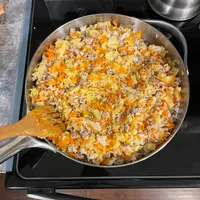 Customer-uploaded image. Click to see more details. The image represents: A large skillet on a stovetop containing a cooked mixture of ground meat, diced carrots, onions, and other vegetables with a wooden spoon