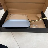 Customer-uploaded image. Click to see more details. The image represents: A light blue ceramic griddle pan with gold handle displayed in an open cardboard box on a tiled floor