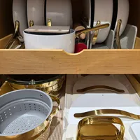 Customer-uploaded image. Click to see more details. The image represents: Organized kitchen cabinet shelves displaying white cookware with gold handles on the top shelf and gold-colored pots and steamers on the bottom shelf