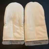 Customer-uploaded image. Click to see more details. The image represents: A pair of beige protective oven mitts with "Caraway" branding on a dark surface