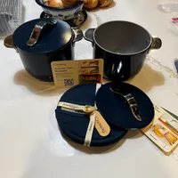 Customer-uploaded image. Click to see more details. The image represents: A set of dark blue Caraway cookware including pots with lids displayed on a white marble countertop, with onions in a decorative bowl and warranty information visible