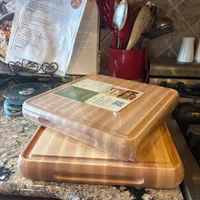 Customer-uploaded image. Click to see more details. The image represents: Two wooden cutting boards stacked on a granite kitchen counter, with kitchen utensils in a red container and recipe papers visible in the background