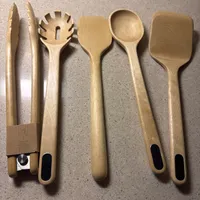 Customer-uploaded image. Click to see more details. The image represents: Six wooden kitchen utensils arranged on a gray speckled countertop, including tongs, a slotted spoon, a spatula, a round spoon, and a paddle, with one item still in its cardboard packaging.