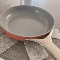 Customer-uploaded image. Click to see more details. The image represents: A coral and cream colored non-stick frying pan with a ceramic interior sits on a speckled gray countertop next to white kitchen towels.