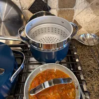 Customer-uploaded image. Click to see more details. The image represents: Kitchen stovetop with blue cookware including a steamer insert and a pan containing red tomato-based sauce with cooking utensils