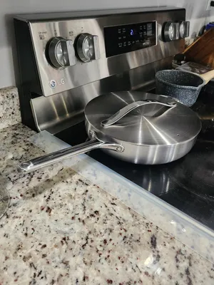 Customer-uploaded image. Click to see more details. The image represents: A stainless steel LG electric stove with two burners on the left, digital controls in the center, and two knobs on the right. A large skillet with lid sits on the stovetop. The stove is positioned on a speckled granite countertop in a kitchen.