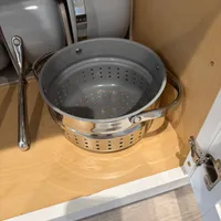 Customer-uploaded image. Click to see more details. The image represents: Stainless steel colander with perforated bottom stored in kitchen cabinet alongside other cookware