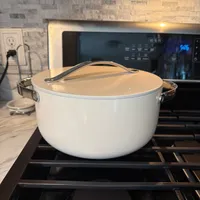 Customer-uploaded image. Click to see more details. The image represents: A white ceramic Dutch oven with lid and handles sits on an oven rack inside an open oven, with a modern kitchen featuring marble backsplash and microwave visible in the background.