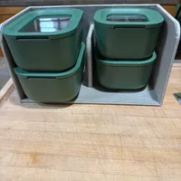 Customer-uploaded image. Click to see more details. The image represents: Four green storage containers with transparent lids arranged in a gray fabric organizer box on a wooden table, with a kitchen counter and cabinets visible in the background.
