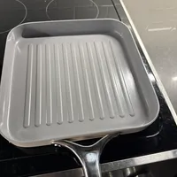 Customer-uploaded image. Click to see more details. The image represents: A square grill pan with ridged bottom sitting on a black stovetop with control knobs visible below