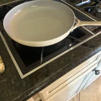 Customer-uploaded image. Click to see more details. The image represents: A white ceramic skillet with a long handle sits on a black electric stovetop in a kitchen with dark granite countertops.