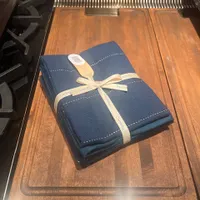 Customer-uploaded image. Click to see more details. The image represents: Blue napkins tied with cream ribbon on wooden cutting board in kitchen