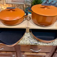 Customer-uploaded image. Click to see more details. The image represents: Orange cast iron Dutch ovens with lids on wooden trivets, alongside black skillets on a granite kitchen counter