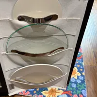 Customer-uploaded image. Click to see more details. The image represents: A fabric storage organizer with multiple compartments holding various plates and dishes, placed on a wooden floor next to a colorful patterned rug