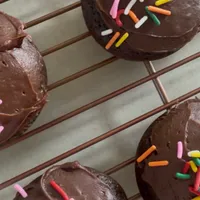 Customer-uploaded image. Click to see more details. The image represents: Chocolate cupcakes with chocolate frosting decorated with colorful sprinkles, arranged on a cooling rack.