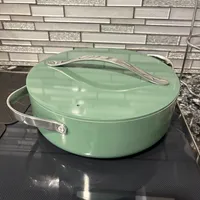 Customer-uploaded image. Click to see more details. The image represents: A mint green ceramic Dutch oven with lid and silver handles sitting on a black stovetop against a gray and white tile backsplash