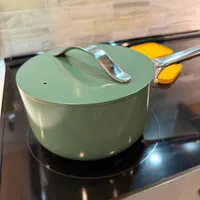 Customer-uploaded image. Click to see more details. The image represents: A green pot with lid and handle sitting on a black induction cooktop with yellow control buttons
